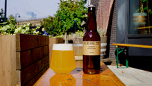 Load image into Gallery viewer, A bottle of The Kernel Brewery - Grisette and a glass of golden beer with white foam, set on a wooden bench outside of the Spa Road Taproom