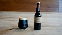 Load image into Gallery viewer, Dark beer bottle and glass on a wooden surface with a blurred background
