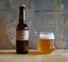 Load image into Gallery viewer, Bottle and glass of beer labeled &#39;The Kernel&#39; on a wooden surface with a concrete wall background.
