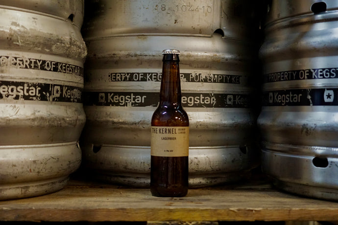 Beer bottle labeled 'The Kernel' in front of metal kegs with 'Kegstar' branding.