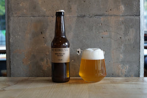 Beer bottle and glass with foam on a wooden surface against a concrete wall.
