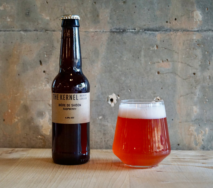 Bottle and glass of raspberry beie de saison from The Kernel Brewery on a wooden surface with a concrete wall background