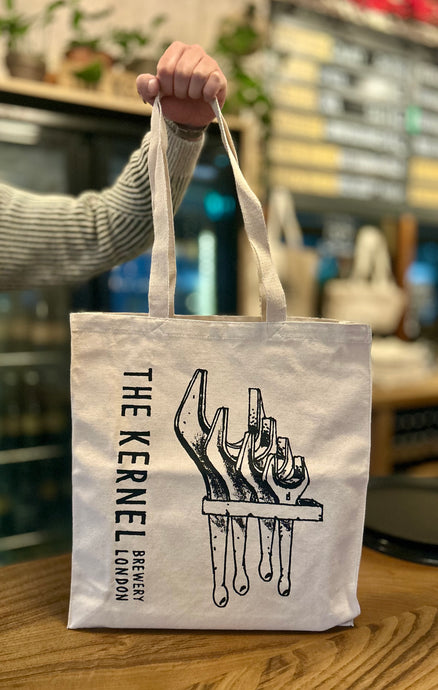 Tote bag with 'The Kernel Brewery London' design held by a person in a blurred indoor setting.