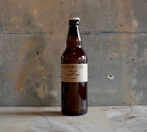 A single 500ml bottle of The Kernel Brewery Pale Ale - Citra, HBC 1019, Sabro stood on a wooden table infront of a concrete wall