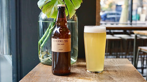 A bottle and pint of The Kernel Brewery's Table Beer sat on a wooden bench.