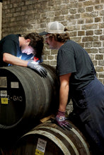Load image into Gallery viewer, Two people working with barrels against a brick wall.
