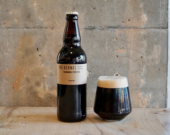 Dark beer bottle and glass on a wooden surface with a concrete wall background