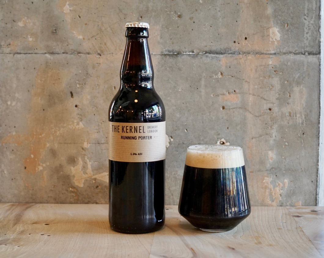 Dark beer bottle and glass on a wooden surface with a concrete wall background