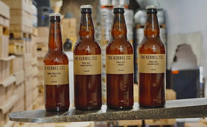 Four bottles of 'The Kernel Brewery' beer stood side-by-side on the prongs of a forklift. 