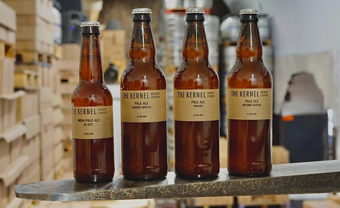 Four bottles of 'The Kernel Brewery' beer stood side-by-side on the prongs of a forklift. 