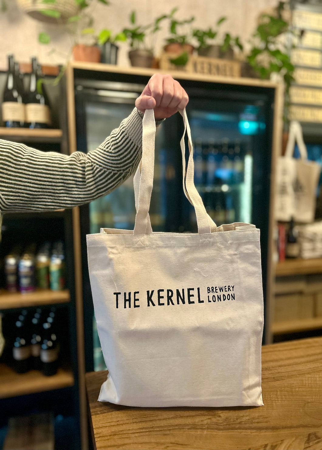 Person holding a tote bag with 'The Kernel Brewery London' branding in a bar setting.