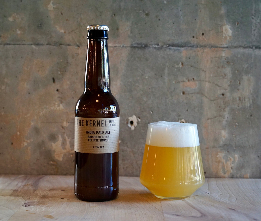Bottle of 'The Kernel' India Pale Ale - Amarillo, Cita, Eclipse, Simcoe with a glass of beer on a wooden surface against a textured wall.