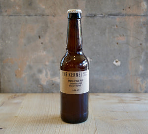 Beer bottle labeled 'The Kernel' on a wooden surface with a rustic background