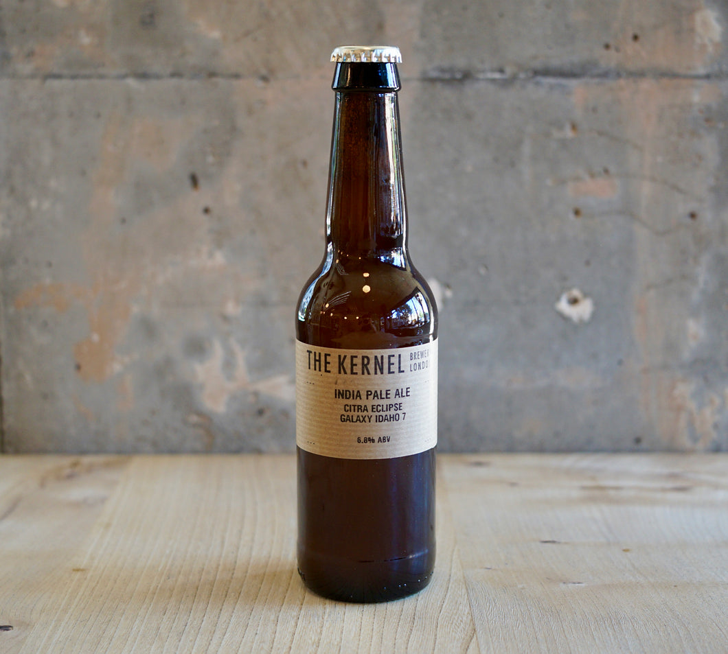 Beer bottle labeled 'The Kernel' on a wooden surface with a rustic background