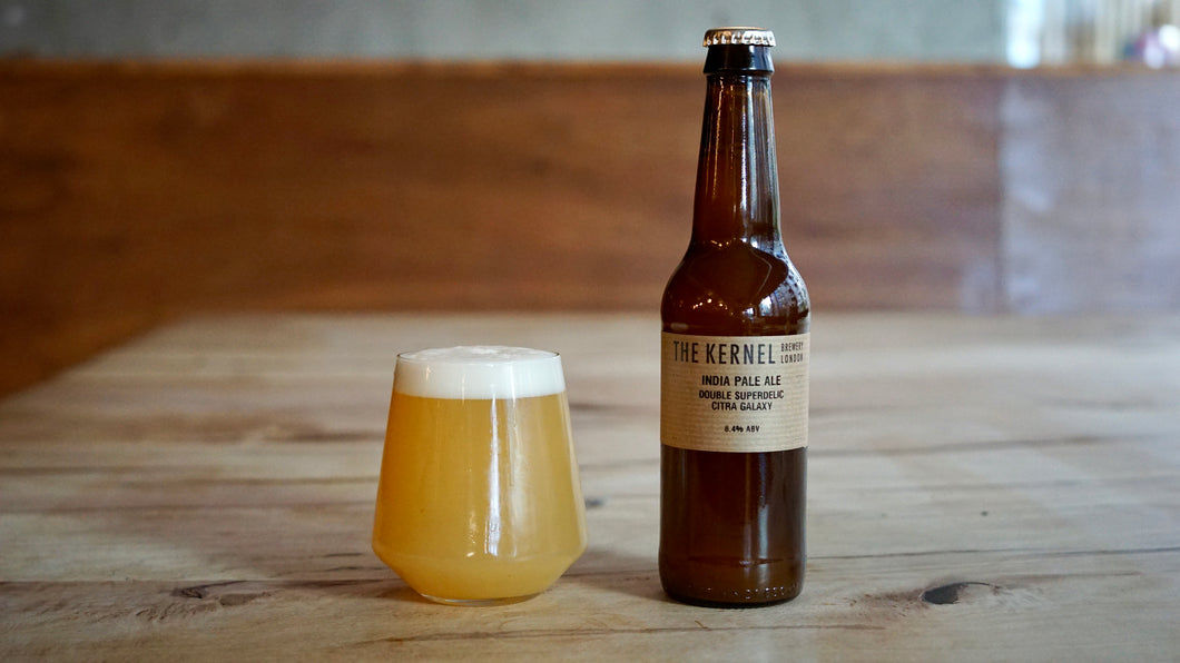 Bottle of India Pale Ale Double Superdelic, Citra, Galaxy from The Kernel Brewery and glass on a wooden table with a blurred background