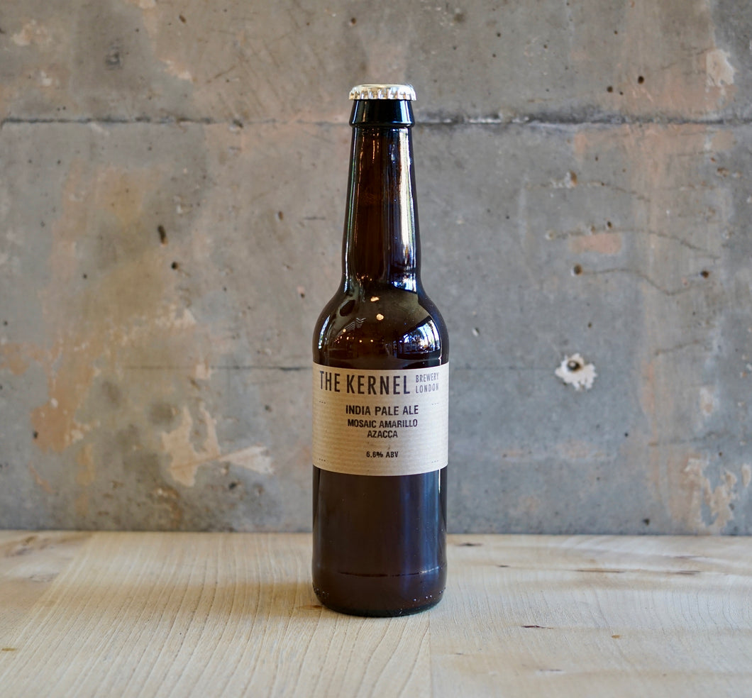 Beer bottle labeled 'The Kernel' on a wooden surface with a rustic background