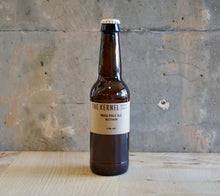 Load image into Gallery viewer, Beer bottle labeled &#39;The Kernel&#39; on a wooden surface with a concrete wall background
