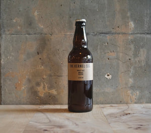 A single 500ml The Kernel Brewery Pale Ale - Mosaic, Eclipse bottle stood on a wooden tabl in front of a concrete wall. 