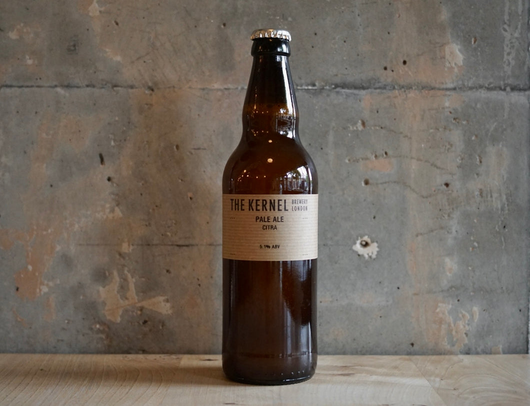 A single bottle of The Kernel Brewery Pale Ale - Citra (500ml). It is stood infront of a concrete wall. 