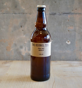 Beer bottle with 'The Kernel' label on a wooden surface and concrete wall background