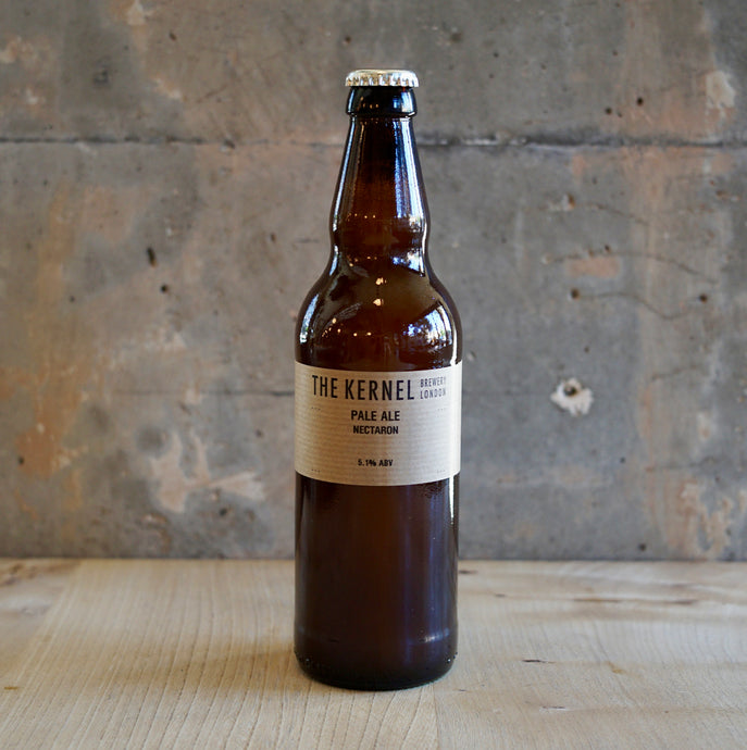 Beer bottle with 'The Kernel' label on a wooden surface and concrete wall background
